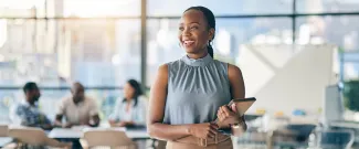 A woman standing and smiling in a busy office building.